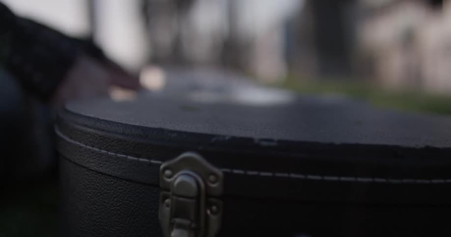 A person is getting a guitar out of a case in a park
