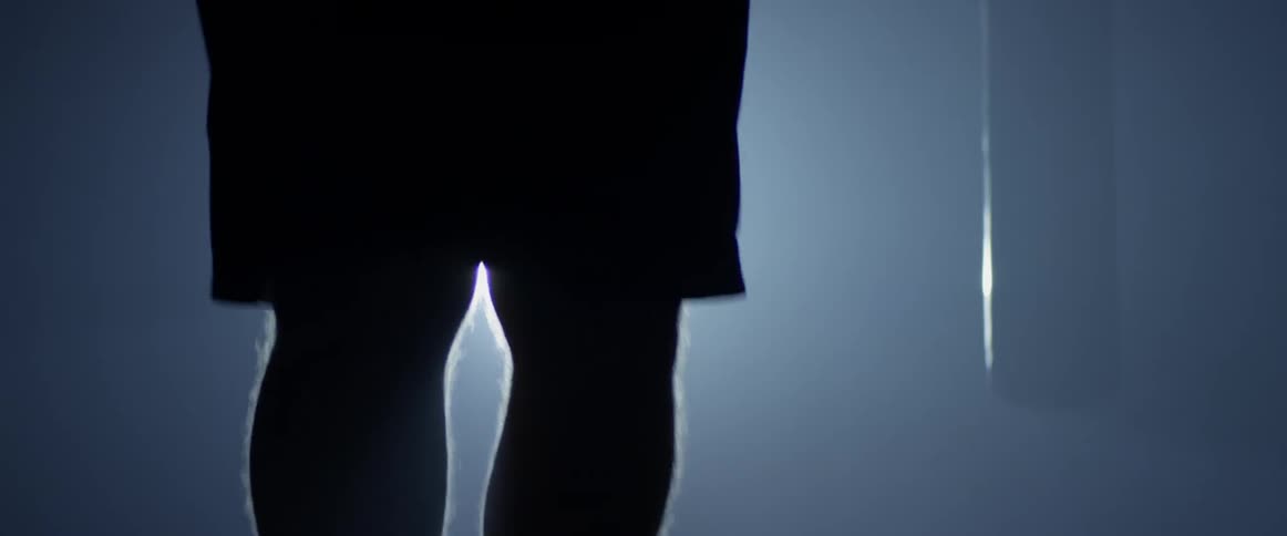 A bright light shines on a man's legs jumping rope