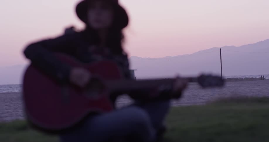 A female strumming a guitar by a body of water