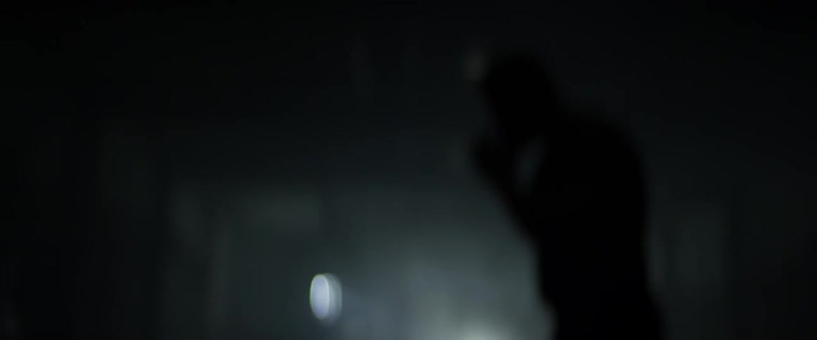 A man practices boxing in a dark room by himself and the camera is kinda blurry