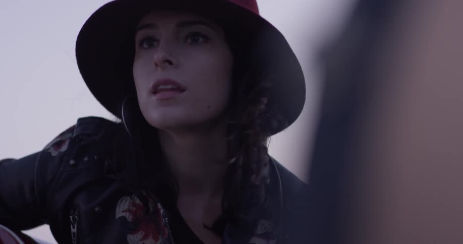 A woman in a hat that is playing a guitar