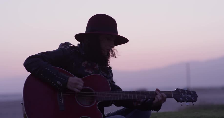 A woman plays guitar in the grass by a beach