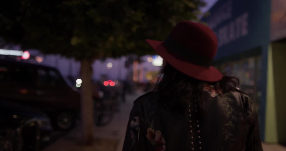 A woman in a hat walking down a sidewalk on a street
