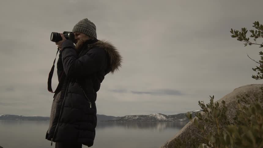 A woman stands in a cold climate of nature and aims her camera at the horizon