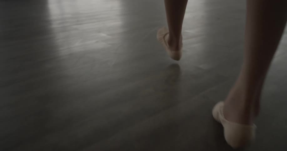 A women walks forward on the wooden floor of a dance studio