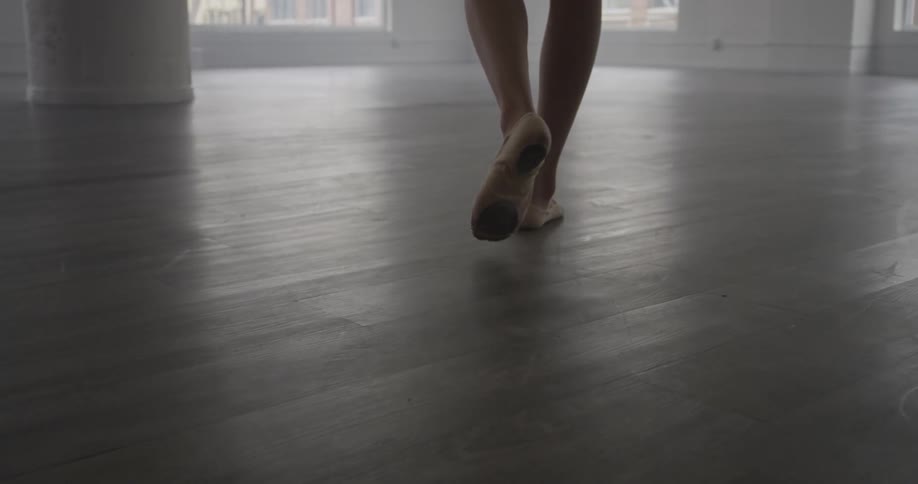 A woman walking across a wooden floor in a dance studio