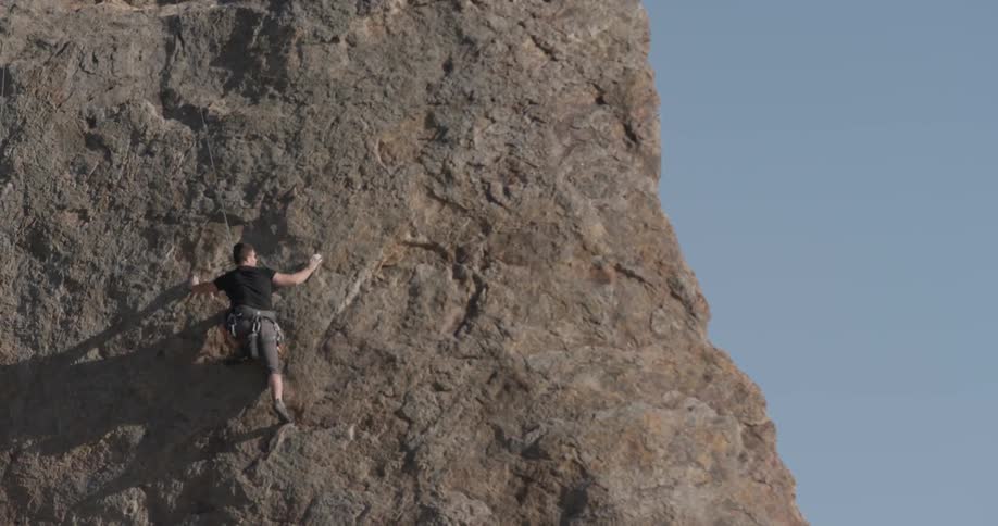 A daring mountain climber scales the face of a huge cliff to enjoy the beautiful day