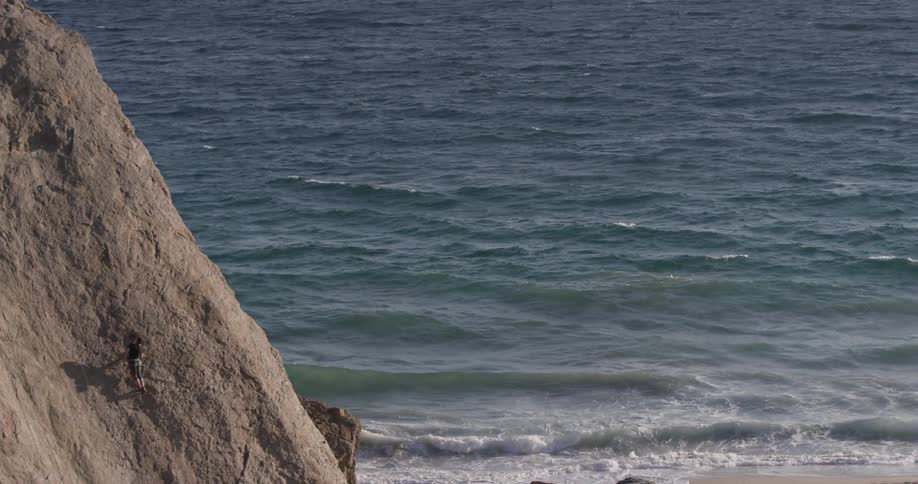 A person climbing up a cliff beside a body of water