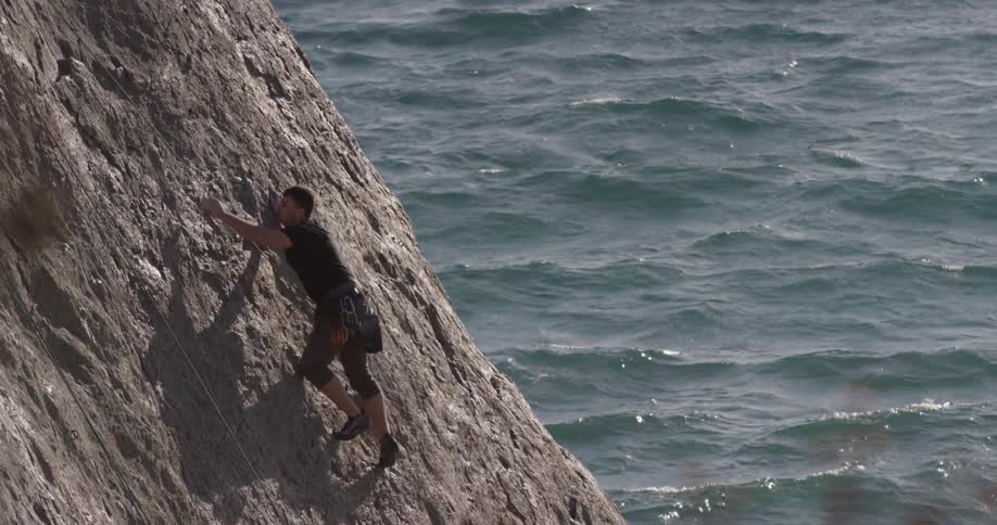 A man is rock climbing above a body over water