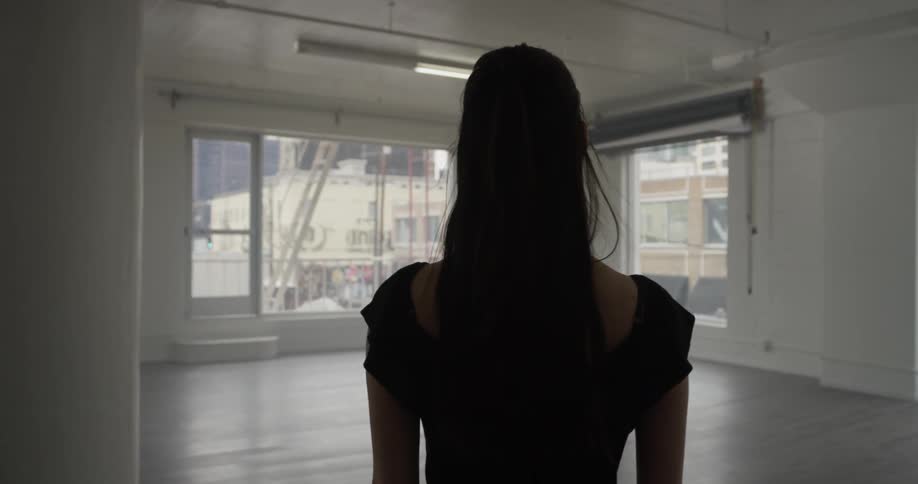 A woman walks along a wooden floor towards windows