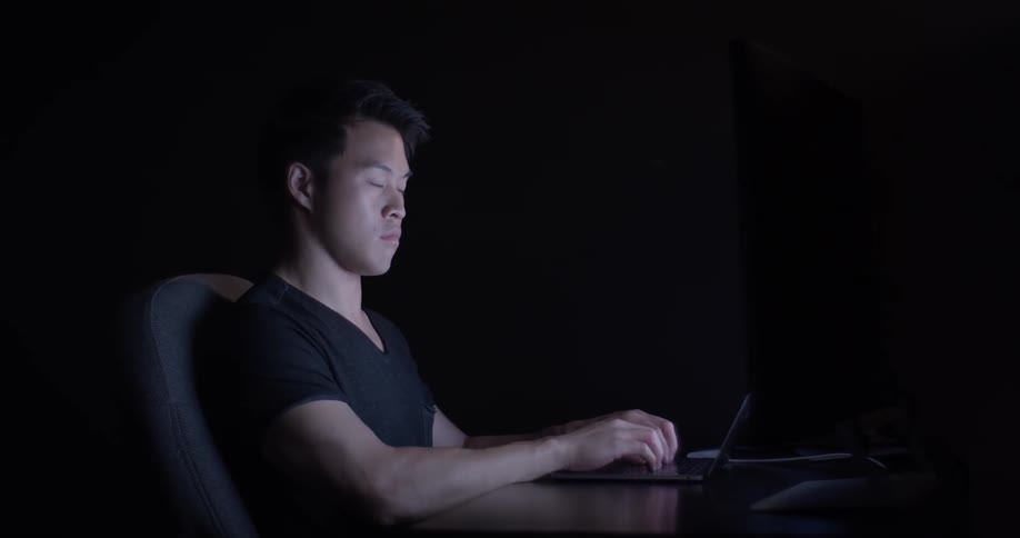 A man typing on a laptop in a dark office