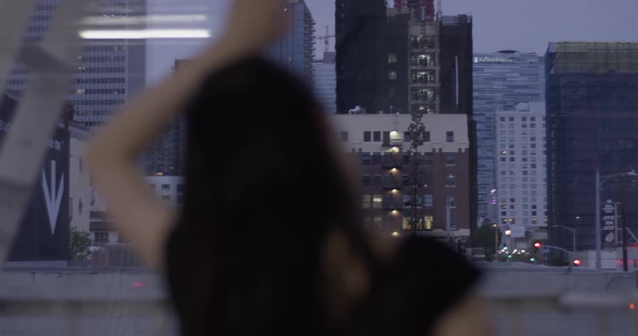 A woman touching a window looking out onto a city at dusk