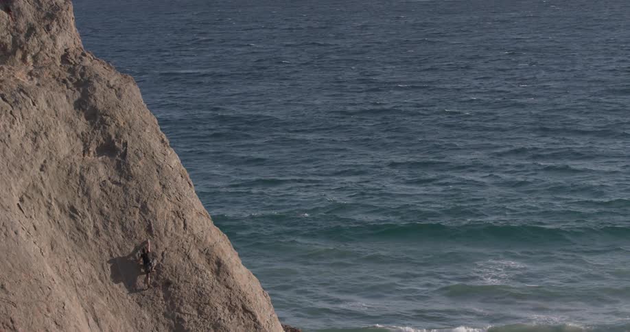 A man rock climbing a very steep mountain by the ocean