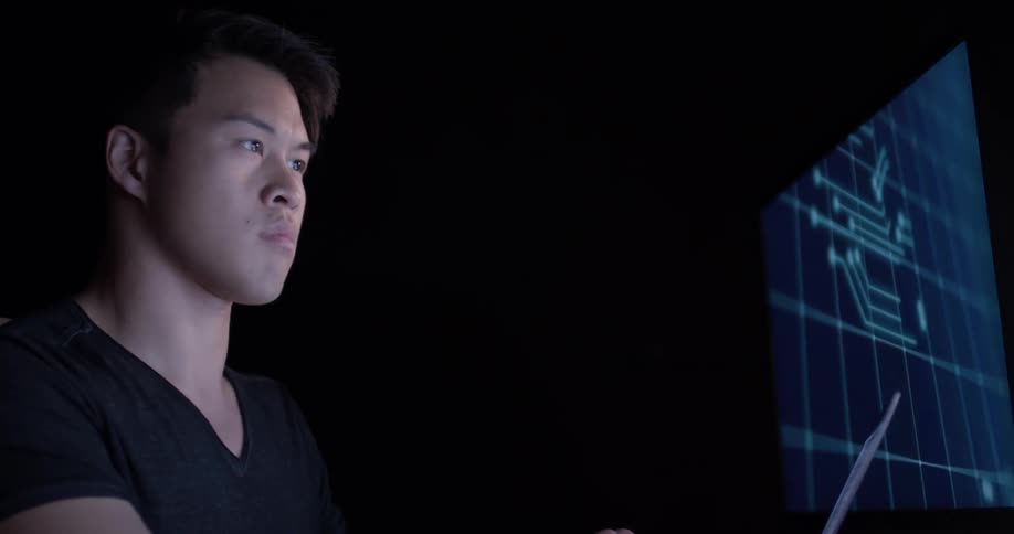 A man sits in the darkness lit only by the light of a computer monitor