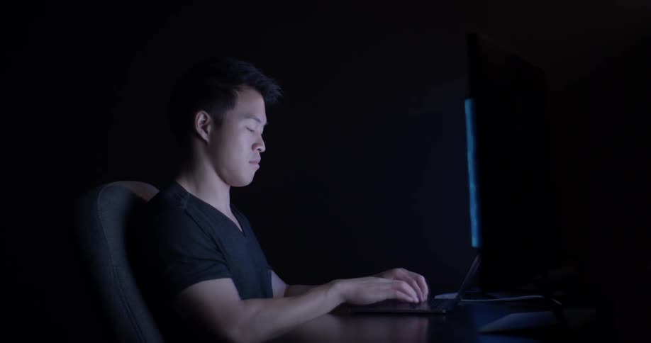 A man is sitting at a desk with a laptop and large screens