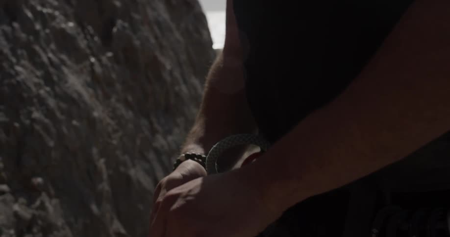 A man with sunglasses is making a rope knot around his waist