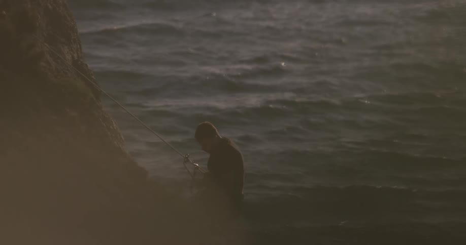 A man repels down a cliff toward the ocean