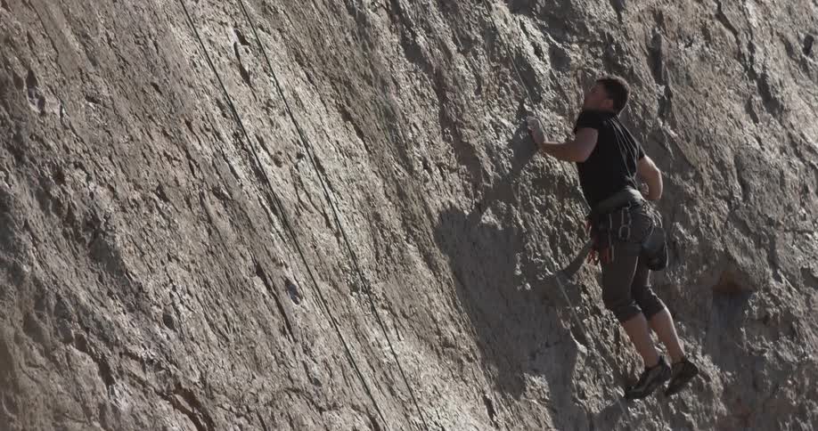 A man uses ropes to assist him up a cliff
