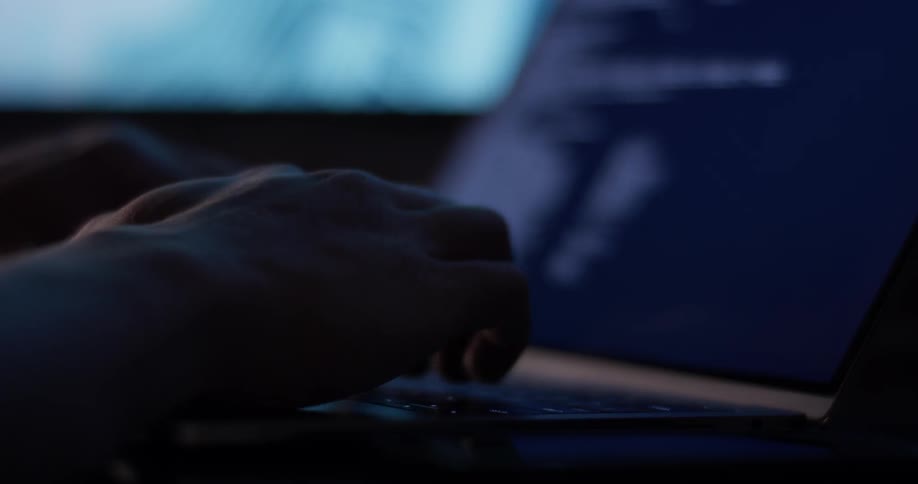 A man typing on a laptop in front of a screen