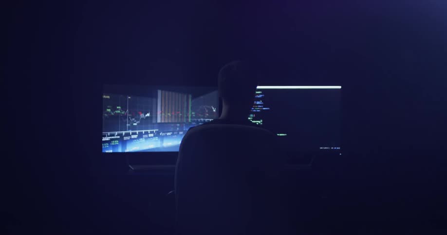 Man looks at two monitors in a dark room