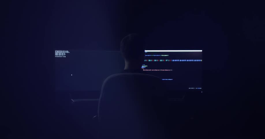 A man is working on a few different monitors in the dark