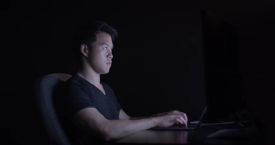A man is sitting down and using his laptop