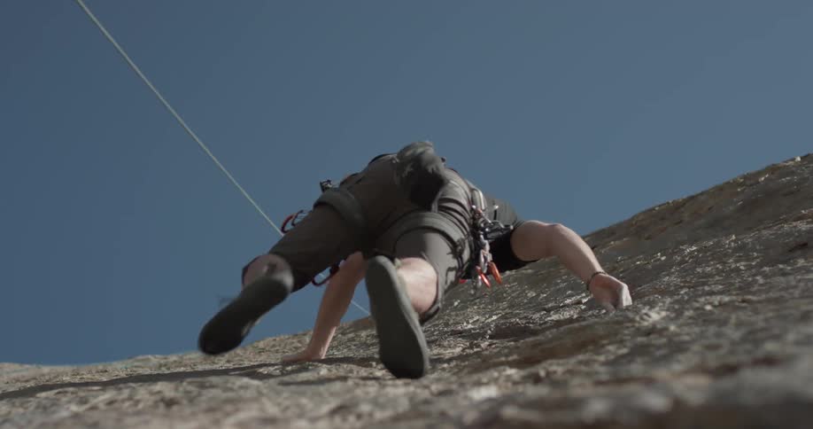 A man climbing up a cliff with ropes