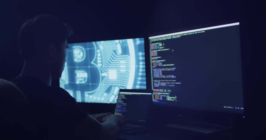 A man sits and works on a laptop that is pushing two monitors
