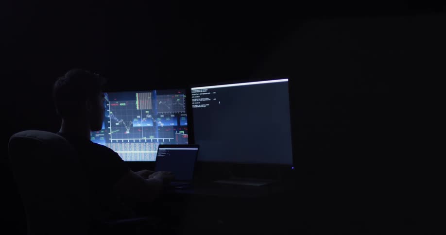 A man is sitting at a desk with large monitors and a small laptop