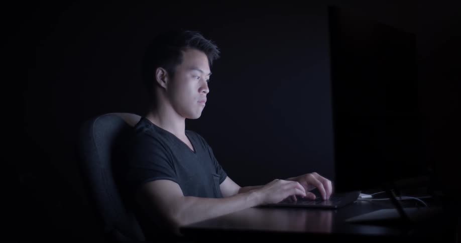 Man typing on keyboard in a dark room