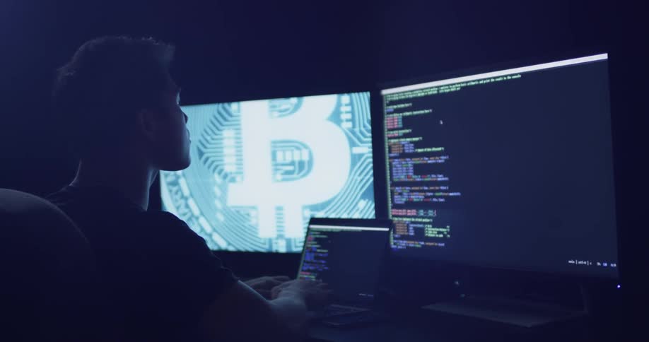 A man is sitting in front of a laptop and two large monitors