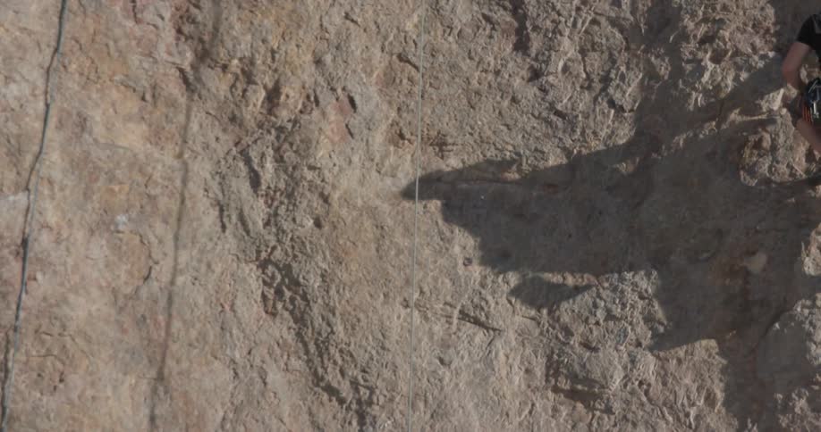 Man scales the side of a rocky cliff on a sunny day