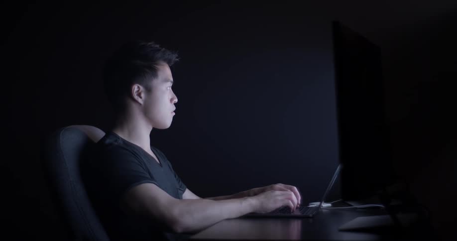 A man that is typing on a computer in a dark room