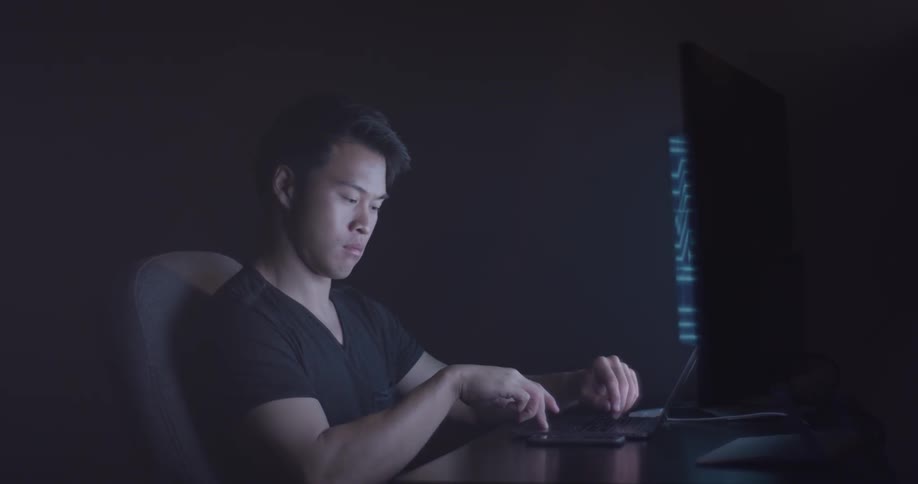 Man in dark room on computer answers his phone