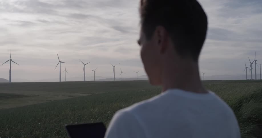 Man standing outside looking at a tablet near windmills
