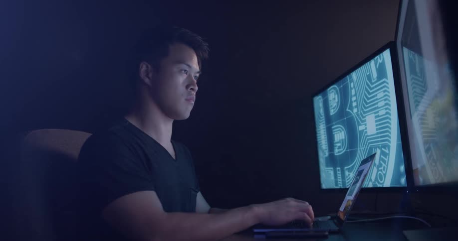 Man surrounded by monitors types on his laptop