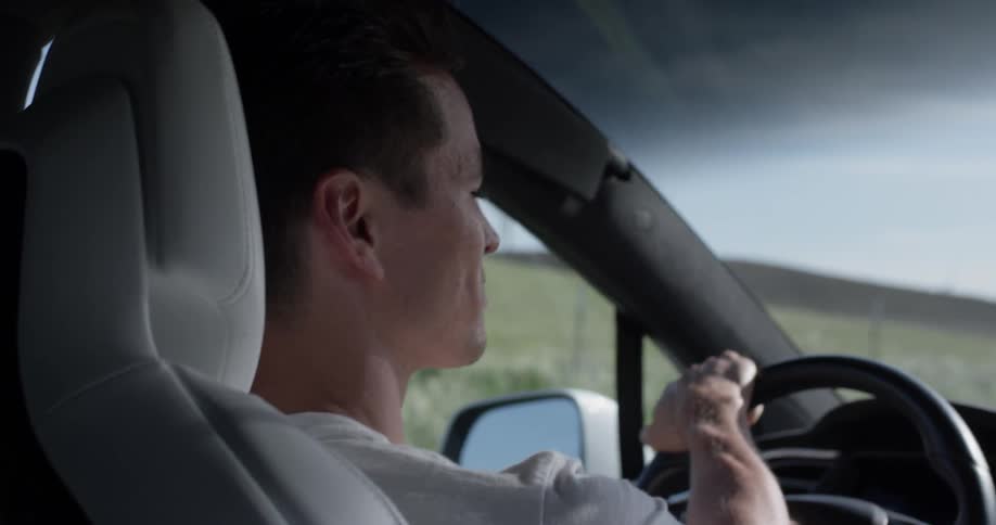 A man driving a car down a dirt road next to a field