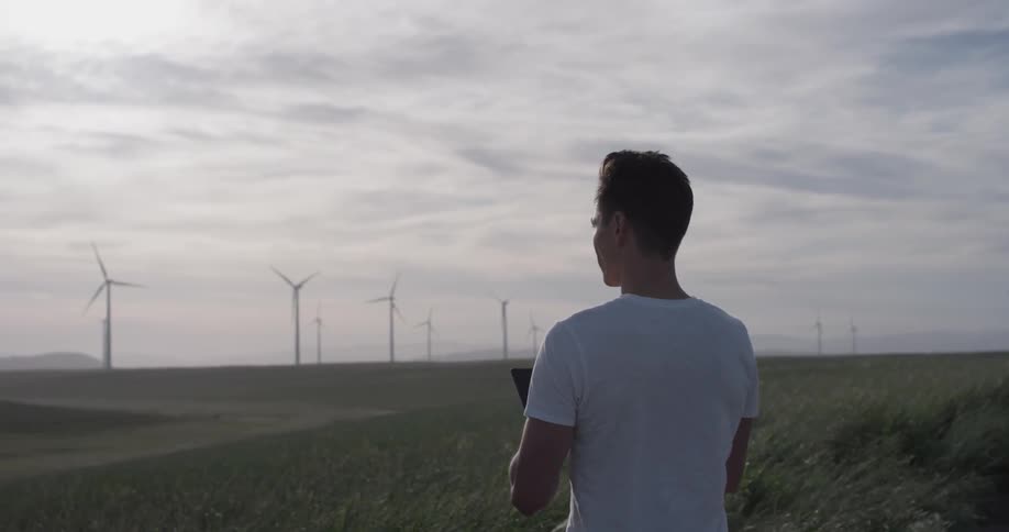 A man that is flying a drone near some windmills