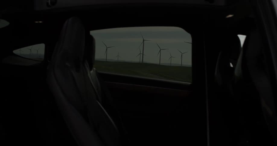 Man Driving Electric Car Through Wind Farm