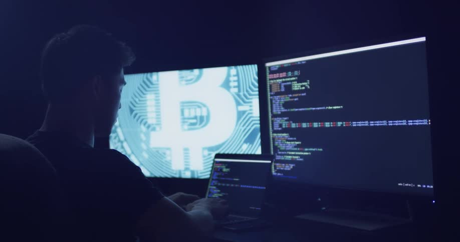 Man types on a laptop sitting in front of two monitors