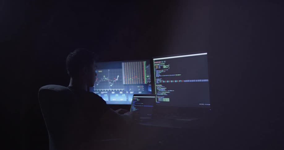 Man sits at desk with two monitors typing on laptop