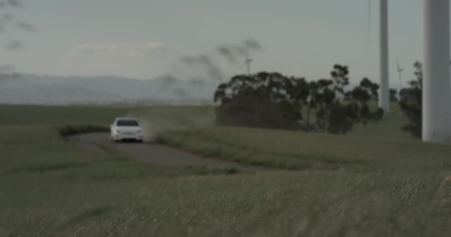 Man Driving Electric Car Through Wind Farm
