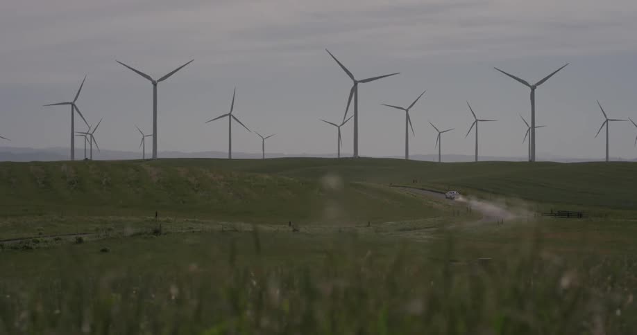 Wind turbines spinning in the distance with a car driving past