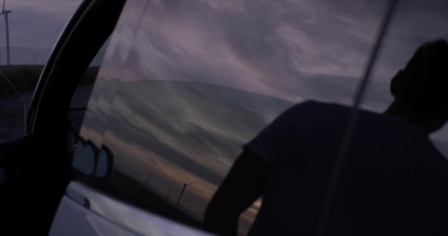 Man Driving Electric Car Through Wind Farm