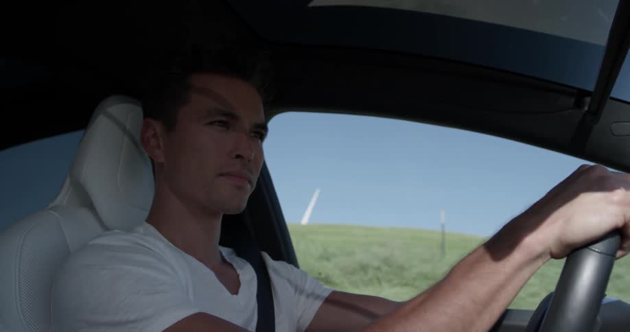 A man driving a car next to a grassy hill