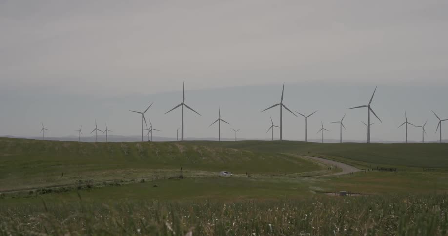 A car driving down a dirt road near some windmills