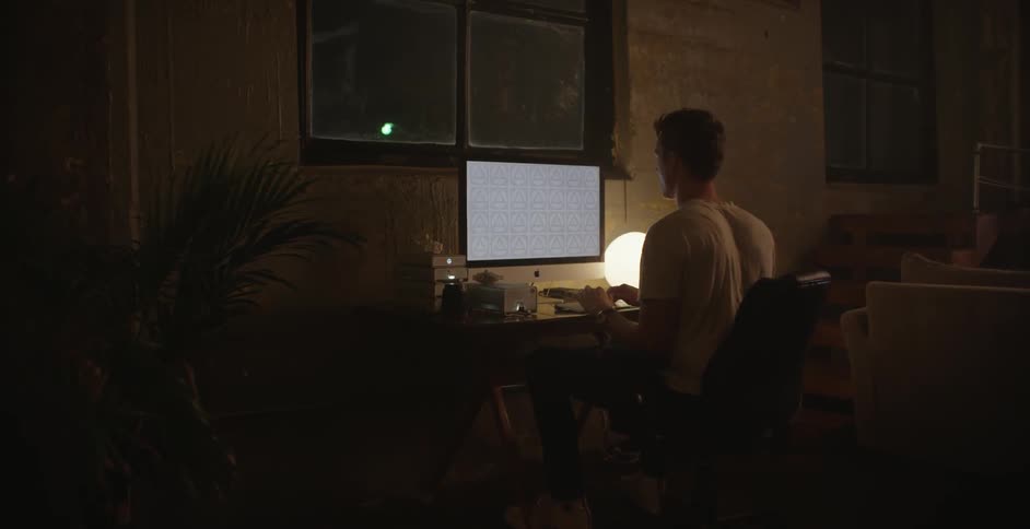 A man sits at his desk at night and works on his apple computer