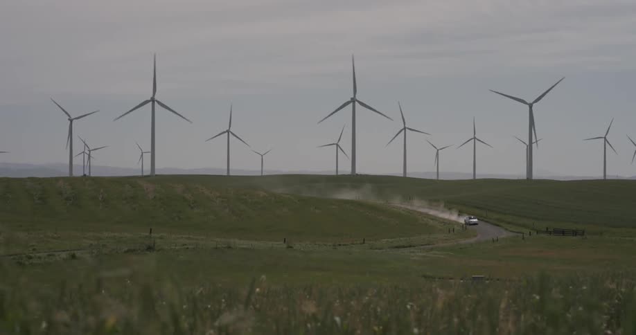 A car driving down a dirt road next to windmills