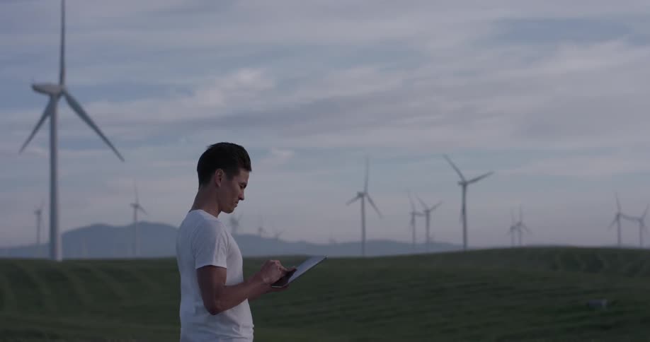 A man with a tablet is standing in a field of wind turbines