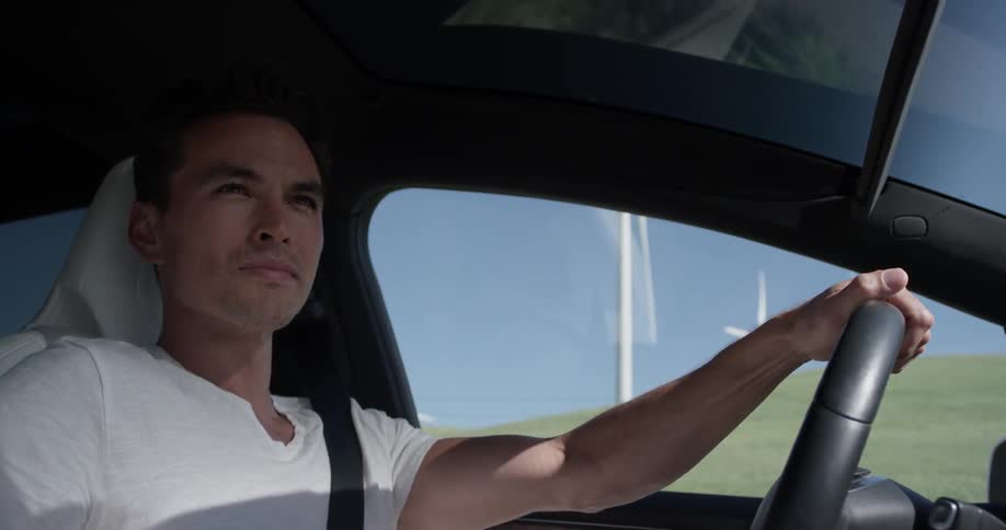 A man drives in a car past windmills